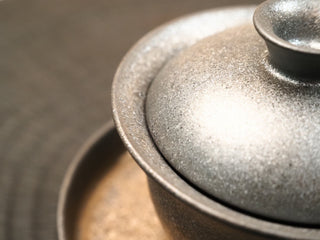 Edge detail of wood-fired stoneware gaiwan lid from Dehua Fujian showing the speckled kiln-change glaze and rim texture.