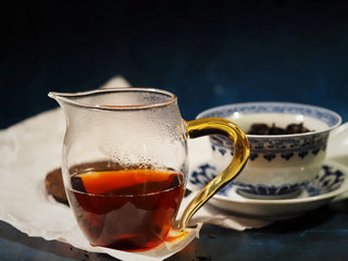 Freshly brewed Yunnan Red Glow Ripe Pu-erh Tea Mini Cake – 100g being poured from gaiwan into a glass gongdao-bei fair cup, revealing its bright ruby-red tea liquor.