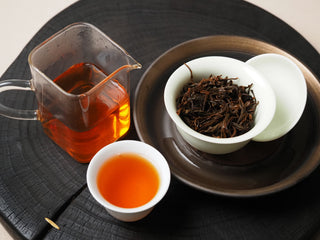 Brewed Yunnan Shaken-Leaf Black Tea leaves alongside a glass pitcher and a cup of bright amber tea liquor.