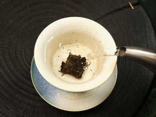 Boiling water poured into a white gaiwan over 2014 Fuding Shou Mei waffle cake section, leaves beginning to infuse, top view.