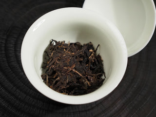 Prised dry tea leaves of 2016 Dayi 7532 Sheng Puerh in a white porcelain Gaiwan bowl, ready for brewing.