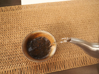 Silver kettle pouring boiling water over Jing Chang Hao Quiet Years 2018 raw Pu-erh leaves in a rustic ceramic cup for the rinse