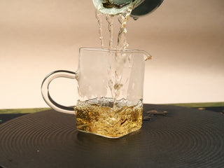 Deep amber tea liquor being poured from a gaiwan into a glass fairness pitcher after brewing Fortune Shou Mei.