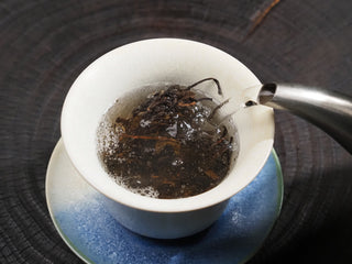 Hot water being poured into a white gaiwan containing Dayi 7542 raw puerh tea leaves to wake the tea.