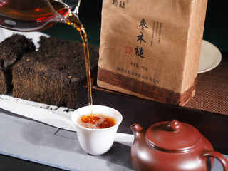 A traditional tea tasting set featuring the 2019 Genshe Fu Brick liquor, a white tasting cup, and a teapot.
