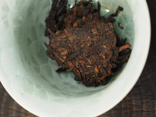 Dry pried leaves of Dayi 7592 ripe puerh tea placed inside a pale green celadon Gaiwan before brewing.