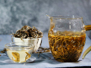 Bright golden yellow tea liquor in a glass server next to dry tea buds.