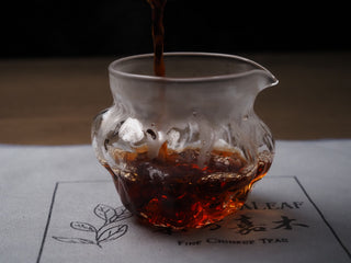 Rich reddish-brown ripe puerh tea soup in a glass gongdao bei (fairness cup) on an Oriental Leaf tea mat.
