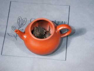 Dry leaves of Jingyang Golden Flower Fu Brick Tea placed inside a purple clay teapot, showing the tea brick fitting and preparation for brewing authentic Chinese dark tea.