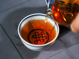 Pouring the brewed 2015 Genshe Fu Brick tea into a traditional tasting cup, showing its clean and bright infusion.
