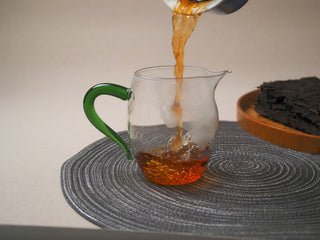 Freshly brewed 2013 Lincang Ripe Pu-erh tea being poured from a fairness cup (cha hai) with a green handle.