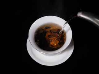 Pouring hot steaming water from a kettle into a porcelain gaiwan with Chenpi Pu-erh tea.