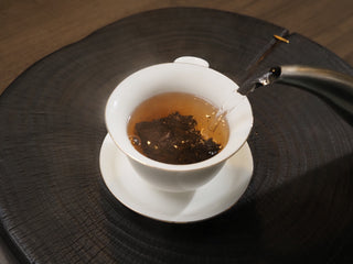 Pouring hot water from a kettle into a white porcelain Gaiwan to brew Dayi 7572 ripe puerh tea.