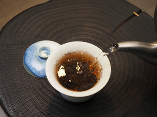 Pouring hot water from a kettle into a Gaiwan to brew 2019 Dayi 7572 ripe puerh tea.