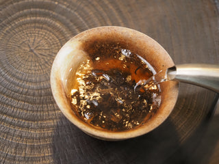 Pouring hot water over 2017 Dayi 7452 ripe puerh tea leaves in a coarse stoneware bowl for brewing.