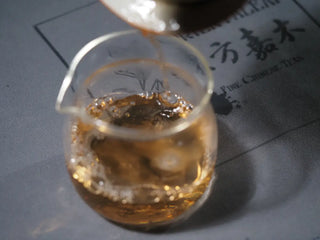 Tea liquor from Sticky Rice Aroma Raw Pu-erh Cake 2013 200g being poured from gaiwan into fair cup