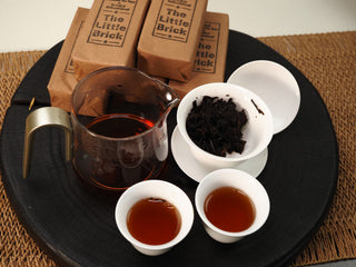 The Little Brick fu brick tea brewing session with glass pitcher, gaiwan with wet leaves and two cups of bright red tea liquor