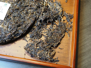 Pried loose leaves and broken sections from the 2005 Lincang vintage raw Pu-erh tea cake on a wooden tea tray.