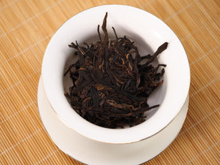 Dry leaves of Jing Chang Hao Mengsong Autumn Harvest 2013 raw Pu-erh in a white gaiwan before brewing, slender dark arbor leaf