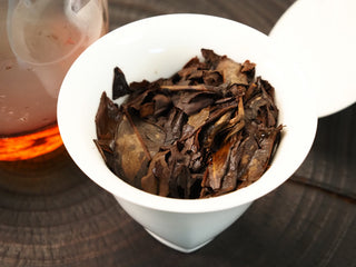 Wet leaf of the 2013 Fuding Shou Mei after brewing, dark brown large leaves in a gaiwan, beside a glass pitcher of red liquor.