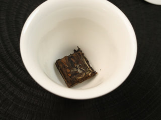 Section of 2014 sun-dried Fuding White Peony waffle cake placed in a white ceramic cup before brewing, top view.