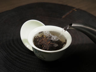 Hot water being poured into a white ceramic Gaiwan with 2016 Dayi 7532 sheng Puerh tea leaves to release its rich aroma.