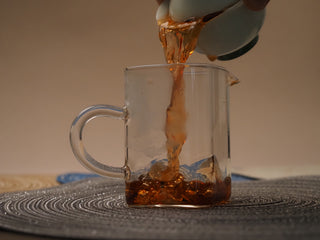 Pouring dark golden liquor of 2018 Dayi V93 ripe puerh tea into a glass pitcher