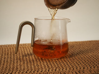 Deep amber liquor of Jing Chang Hao Quiet Years 2018 raw Pu-erh poured from a clay gaiwan into a glass fairness pitcher