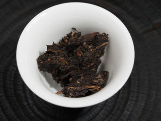 Dry loose leaves of 2021 Dayi Mi Xiang Raw Puerh tea placed in a white porcelain gaiwan before brewing.

