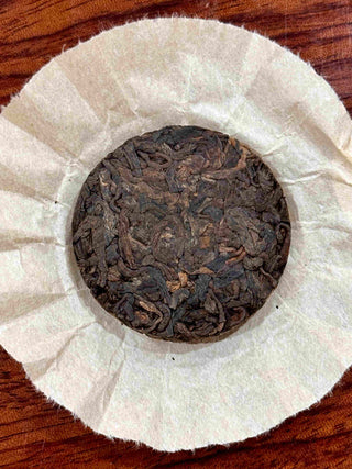 Back of the unwrapped Mengku Rongshi Bingdao Aged Ripe Pu-erh 8g coin cake, tightly pressed dark leaves with golden tips.