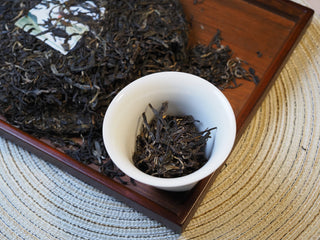 Flat lay display of 2026 Tan Chun raw Puerh tea cake alongside loose dry leaves on a wooden tray.