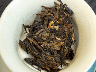 Measured portion of 2006 vintage raw Puerh tea leaves placed inside a white porcelain Gaiwan.