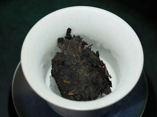 Dry tea leaves of the On Taoism Golden Flower Fuzhuan Tea in a white bowl.
