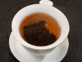 Deep reddish-brown brewed tea liquor of Dayi 7572 ripe puerh inside a white porcelain Gaiwan.