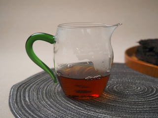 A glass fairness cup filled with the clear, dark red liquor infusion of the 2013 Dry-Aged Lincang Ripe Pu-erh tea.