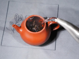 Pouring boiling water into a purple clay teapot with Jingyang Golden Flower Fu Brick Tea, starting the infusion process for traditional dark tea.