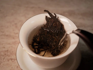 Hot water being poured over 2019 Lincang Ancient Arbor Sheng Pu-erh Tea Cake leaves in gaiwan releasing bright aroma