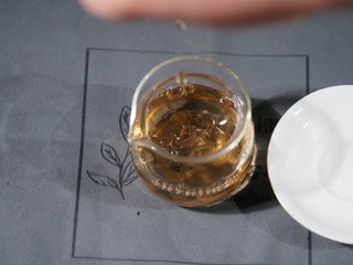 Brewed golden Mengku TeaSoul Sheng Pu-erh Coin Tea being poured from gaiwan into a gongdao cup