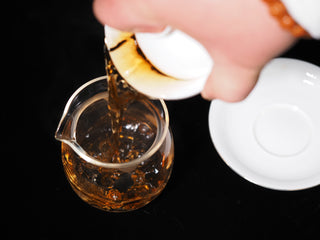 Pouring clear red-brown citrus Pu-erh tea liquor from a gaiwan into a glass Gongdaobei (fairness cup).