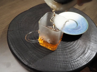 Pouring the freshly brewed golden tea soup of Dayi 7542 raw puerh from a gaiwan into a glass pitcher.