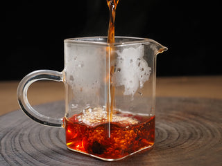 Streaming deep, clear amber-red ripe puerh tea liquor into a glass fairness pitcher (Cha Hai).