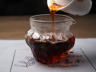Pouring clear and bright amber-red ripe puerh tea soup into a glass server, showing its rich texture.
