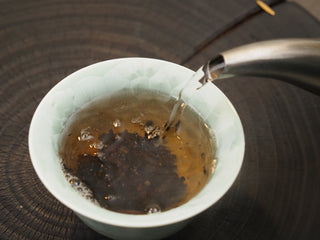 Pouring hot water from a kettle into a celadon brewing bowl to steep 2019 Dayi 7592 ripe puerh tea.