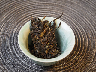 Dry loose leaves of 2025 Tan Chun raw Puerh tea displayed inside a traditional white tasting cup.