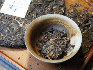 Dry loose leaves of the 2005 Lincang Sheng Pu-erh tea resting inside a handcrafted ceramic tasting cup.