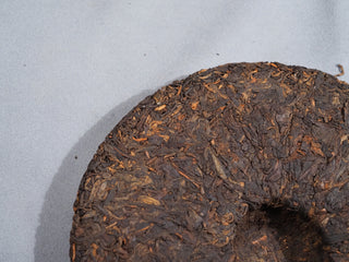 Aged dry leaves and golden buds on the edge of 2006 Dayi 7572 ripe Puerh tea cake