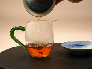 Second steep of 2014 Fuding Shou Mei waffle cake poured into a glass pitcher with green handle, deeper red-brown liquor.