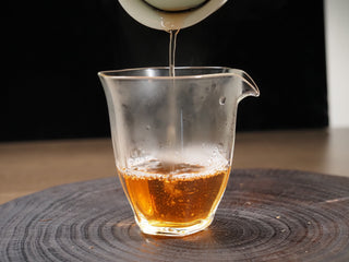 Clear, amber-golden liquor of brewed 2016 Dayi 7532 raw Puerh tea being poured into a glass sharing pitcher (Gongdao Bei).