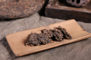 Broken pieces of the 2019 Bojun 500g cake scattered on a wooden tray, showing dark fermented leaves with golden tips.