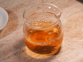 Amber-hued tea liquor from 2019 Qilin Tribute Sheng Pu-erh Tea Cake – Ancient Arbor 357g being poured from gaiwan into a glass gongdao cup.